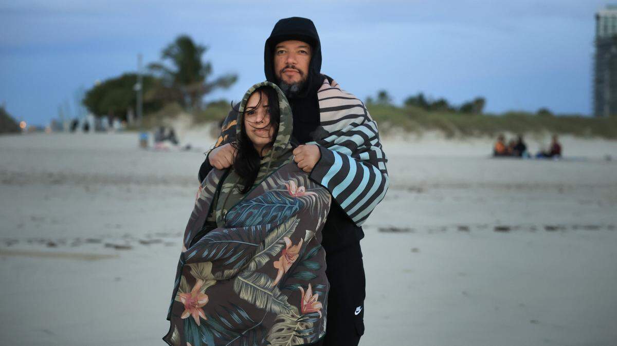 MIAMI BEACH, FLORIDA - NOVEMBER 11: Willie Gonzalez and Lee Gonzalez (front) bundle up against the chilly air as they watch the sunrise on the beach on November 11, 2025 in Miami Beach, Florida. A cool blast of air moved through the area in the morning with temperatures in the upper-40s all across South Florida, and with wind chill it was in the low- to mid-40s. (Photo by Joe Raedle/Getty Images)