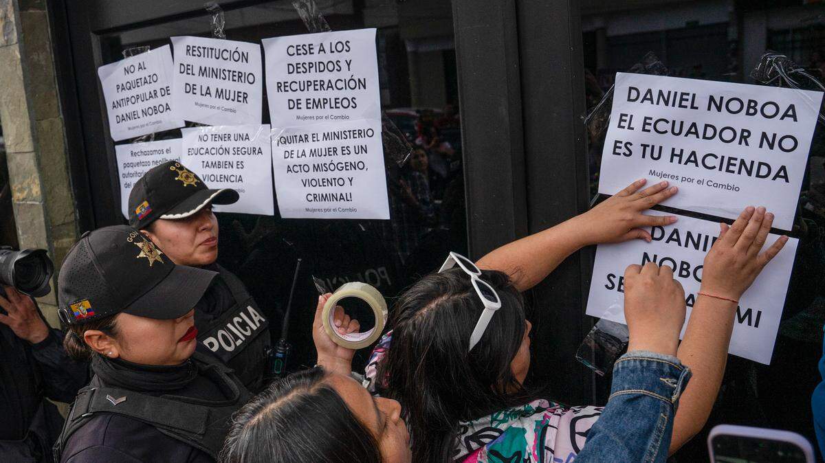 Foto del 28 de julio de 2025 que muestra a varias personas intentando pegar afiches en una puerta de un edificio del gobierno, mientras agentes policiales intentan disuadirlas, en Quito, Ecuador. La protesta era en contra del gobierno del presidente Daniel Noboa.