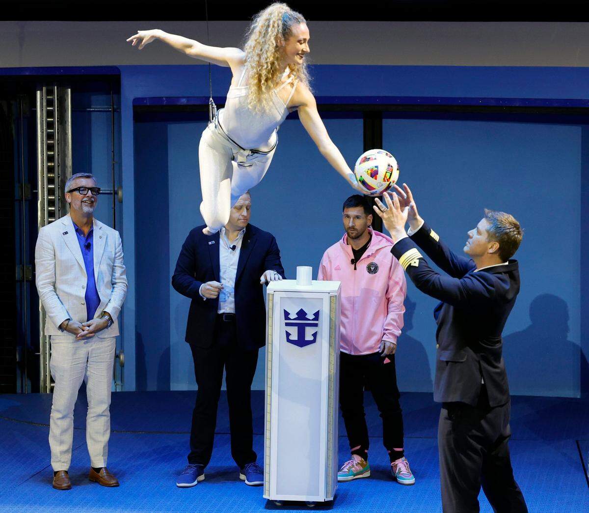 Un artista entrega un balón de fútbol al capitán del crucero Icon of the Seas Henrik Loy, mientras el astro del Inter Miami Lionel Messi observa al fondo, en la ceremonia efectuada el 23 de enero de 2024 en el Puerto de Miami, Florida.