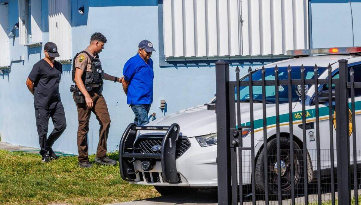 Un policía saca a dos hombres esposados de una casa de Miami-Dade que se utilizaba como clínica veterinaria sin licencia.