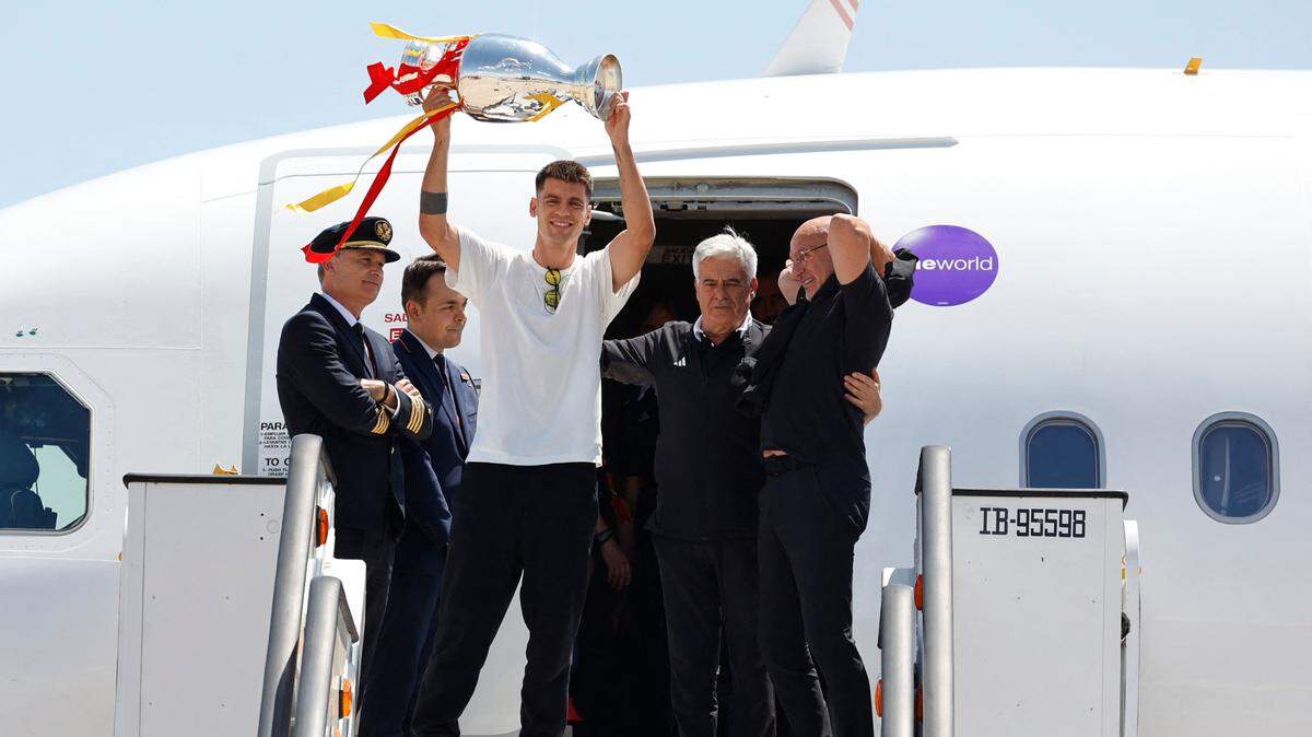 El jugador de la selección española Álvaro Morata levanta el trofeo que su equipo conquistó tras ganar la Eurocopa ante Inglaterra, el lunes en el aeropuerto de Madrid. A su lado Pedro Rocha, presidente de la Federación Española de Fútbol (centro), y el entrenador de la Roja, ​​Luis de la Fuente.
