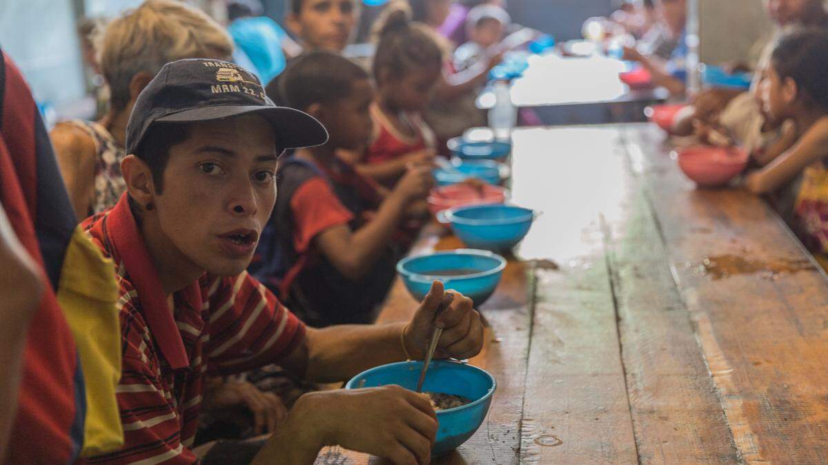 Jóvenes, niños, ancianos y discapacitados se sientan juntos en el comedor de la Casa de María en Propatria, Caracas, para recibir un tazón de sopa.