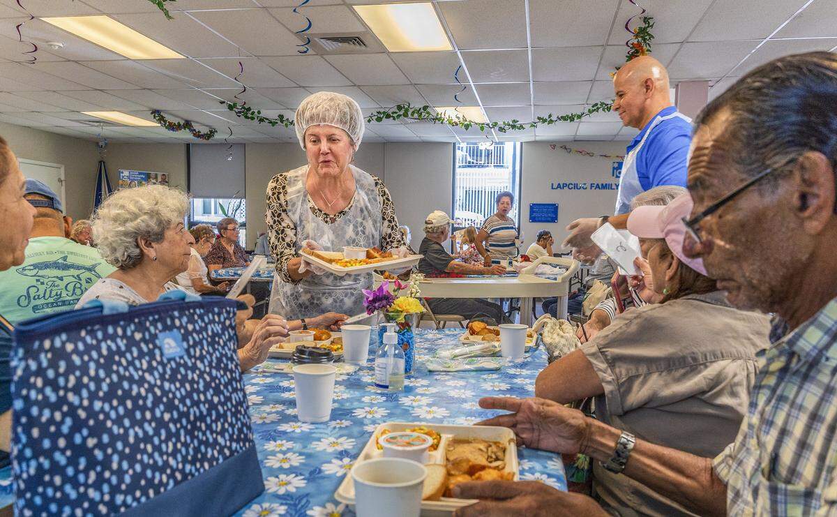 La voluntaria Ana Chica y el empleado Alexander Flores sirvieron comidas durante la hora del almuerzo en el Centro Familiar Diener JCS en Miami Beach. Los servicios podrían verse afectados, ya que JCS es una de las más de 40 organizaciones sin fines de lucro que están perdiendo fondos significativos (16 millones de dólares) debido a los recortes presupuestarios del condado de Miami-Dade, el martes 12 de agosto de 2025.