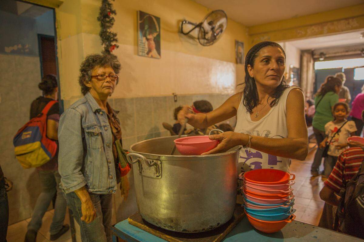 En el comedor de la Casa de María, la cocinera Livia Madueño sirve tazones de sopa. Este comedor benéfico en Propatria, Caracas, sirve unas 350 raciones al día.