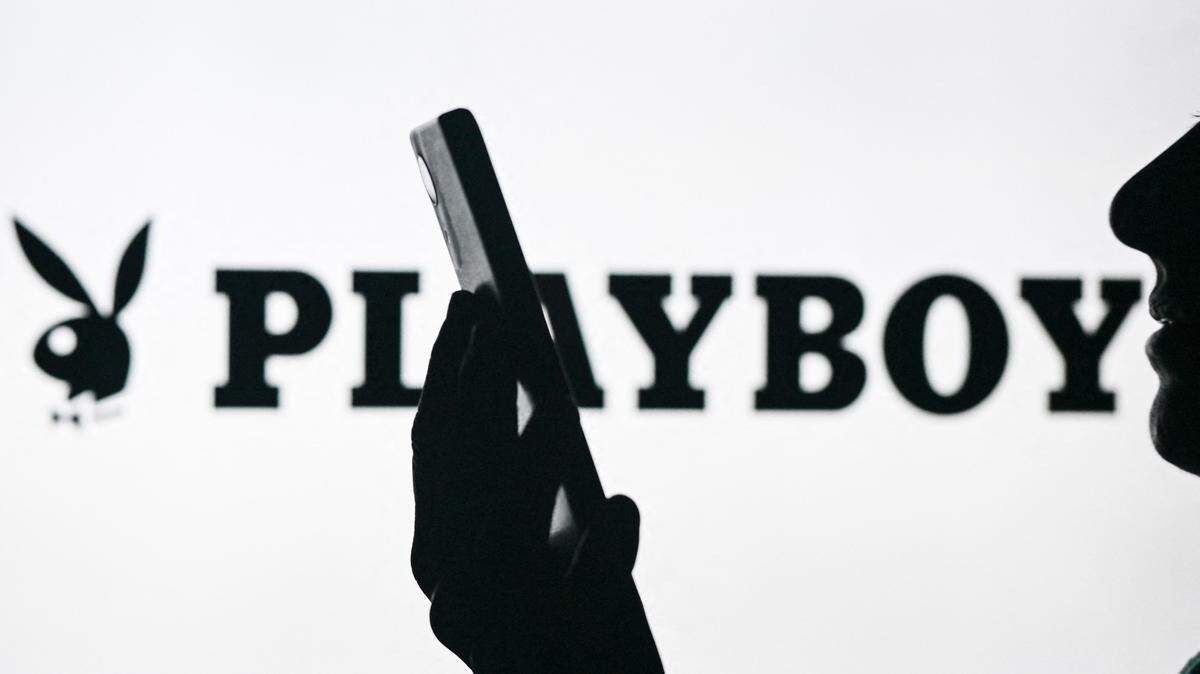 Imagen de una mujer sosteniendo un teléfono celular frente al logo de Playboy mostrado en la pantalla de una computadora, el 29 de abril de 2024, en Edmonton, Canadá.