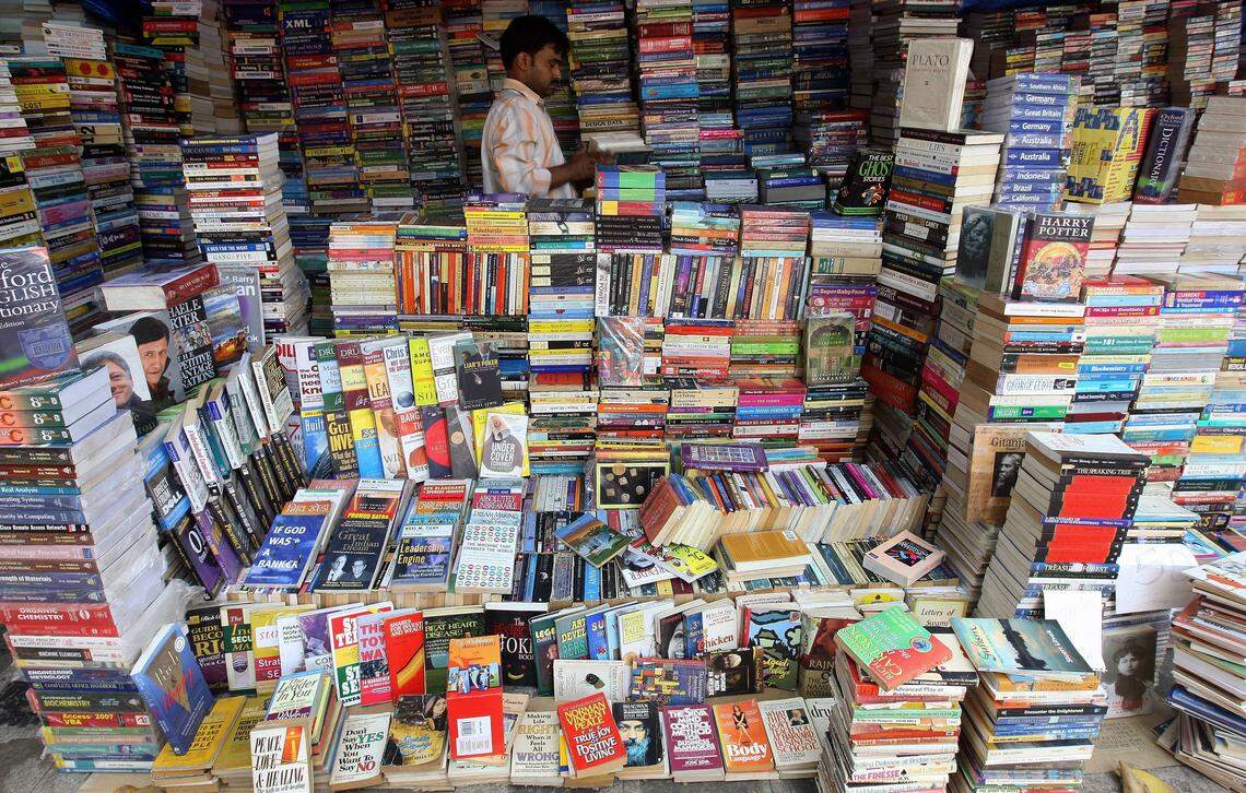 Un librero ordena libros en su puesto callejero, situado junto a una concurrida arteria vial en Mumbai, con motivo del Día Mundial del Libro y del Derecho de Autor.