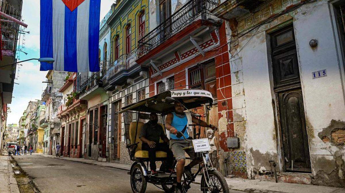 En esta foto de archivo tomada el 27 de octubre de 2021, un bicitaxi recorre una calle decorada con una enorme bandera cubana en La Habana, el 27 de octubre de 2021.(Foto de YAMIL LAGE / AFP a través de Getty Images)