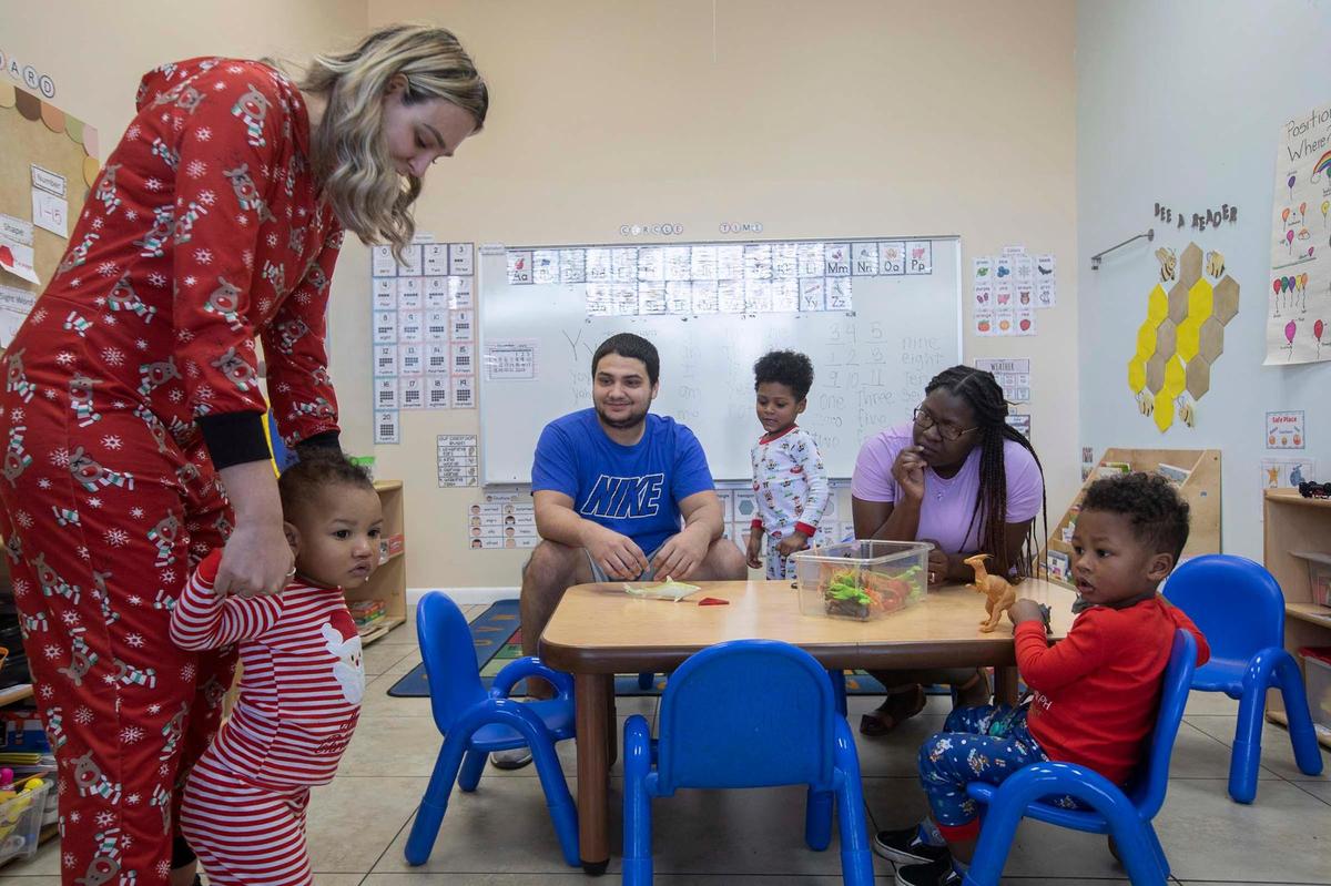 Shazira Álvarez, asistente de dirección, lleva a Miles De Paz, de 1 año, a su madre, Montavia De Paz, en Springview Academy of Hialeah, el viernes 23 de diciembre de 2022. El programa Thrive By 5 en Hialeah ofrece ayuda para pagar la guardería a los padres de bajos ingresos económicos. (Atrás) Masón De Paz 4 años, Mateo De Paz 3 años y papá Miguel De Paz.