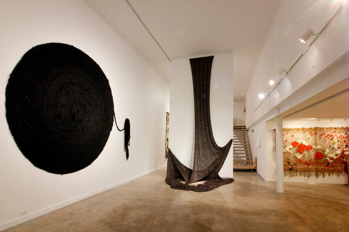 Vista parcial. Izquierda: Akiko Jackson, ‘Herencia tejida’, 2006, 800 pies de pelo sintético entrelazado. Dimensiones y modos de instalación variables. Al fondo: Raquel Schwartz, ‘Woven Channel’, 2008, 300 pies de cinta de casette tejidos. Dimensiones variables.