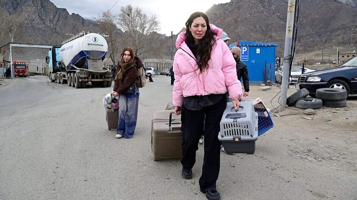 Refugiados iraníes caminan con sus pertenencias tras cruzar la frontera de Irán a Armenia en un puesto de control fronterizo en la ciudad de Meghri, al sur de Armenia, el 8 de marzo de 2026, en plena guerra de Oriente Medio.