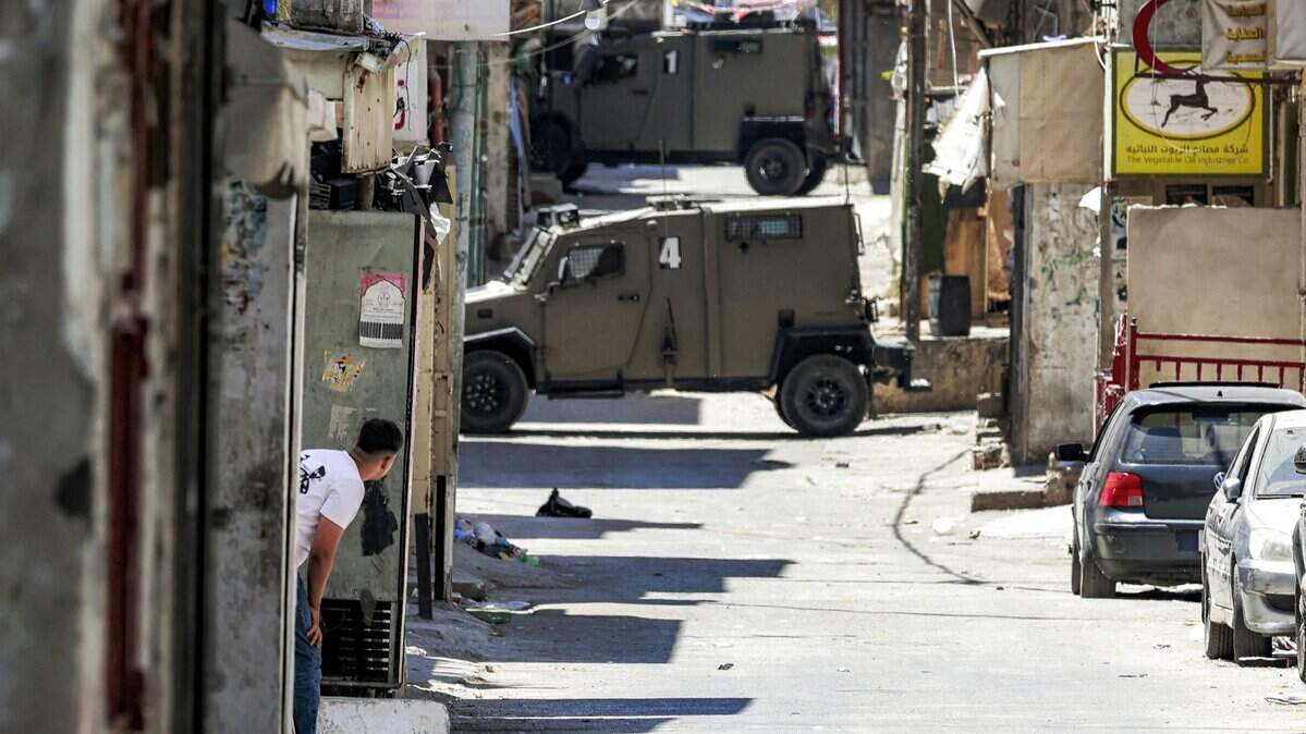 Un hombre se resguarda mientras vehículos blindados del ejército israelí avanzan por callejones del campamento de refugiados palestinos de Balata, al este de Nablus, en la Cisjordania ocupada, durante una operación militar israelí el 7 de junio de 2026.