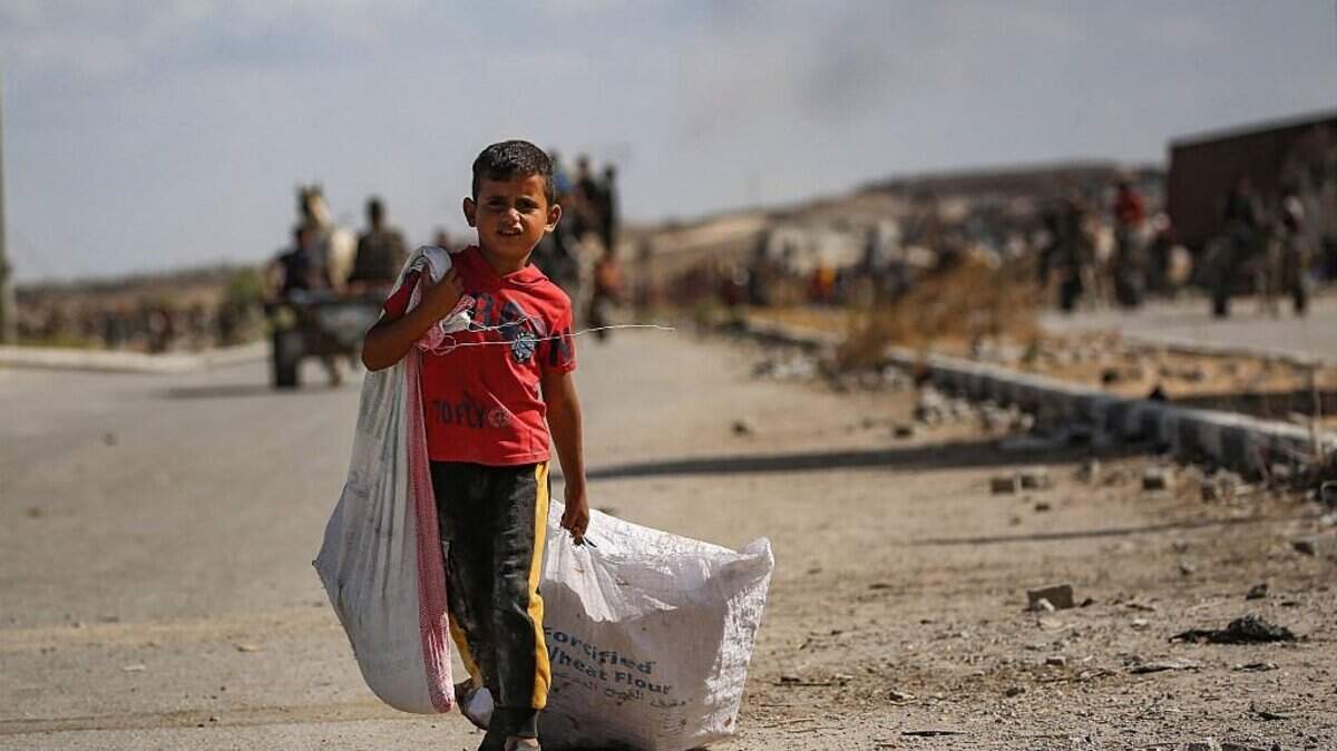 A Palestinian boy carries a bag and drags another behind him as he returns from a food distribution point run by the US and Israeli-backed Gaza Humanitarian Foundation (GHF) group, near the Netsarim corridor in the central Gaza Strip on October 5, 2025. A senior Hamas official on October 5 said the Palestinian militant group is eager to reach an agreement to end the war and implement a prisoner swap with Israel, as negotiators converge in Egypt for talks. (Photo by Eyad BABA / AFP) (Photo by EYAD BABA/AFP via Getty Images)
