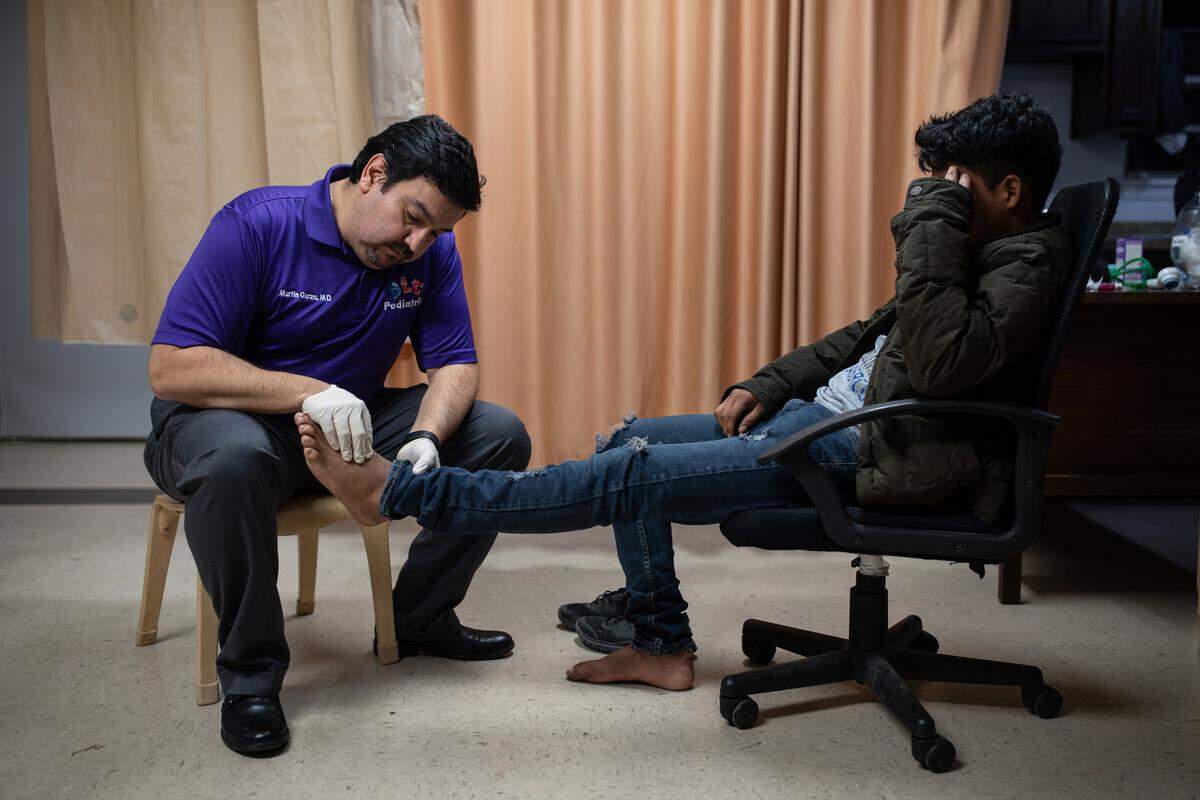 El Dr. Martin Garza, pediatra, examina a Elvin Portillo, de 17 años en la clínica de la Caridades Católicas. Portillo se lastimó el pie durante su travesía desde Honduras.