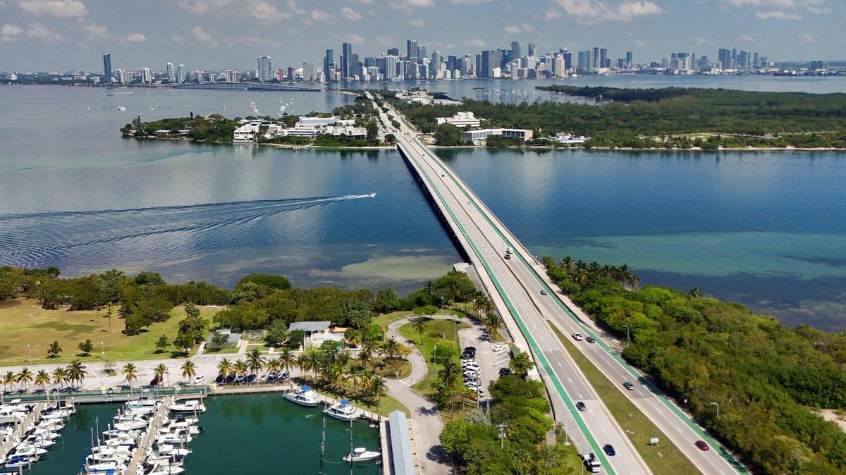 El puente Bear Cut conecta Key Biscayne y el puerto deportivo de Crandon Park (abajo a la izquierda) y la Reserva Bear Cut (abajo a la derecha) con la Calzada Rickenbacker y Virginia Key (arriba al centro). Al fondo se puede ver el horizonte del centro de Miami y Brickell.