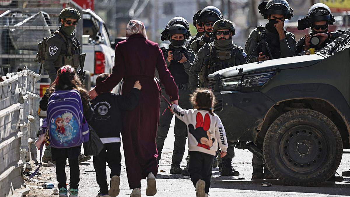 Varios transeúntes pasan junto a miembros de las fuerzas de seguridad israelíes durante una redada militar en el barrio de Kafr Aqab, cerca de Ramallah, en la Cisjordania ocupada por Israel, el lunes 26 de enero de 2026.