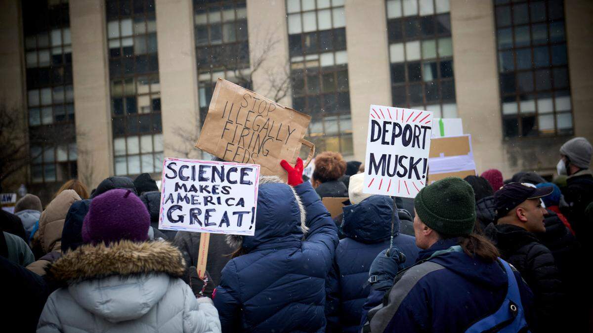 Cientos de exempleados federales, dos ellos con pancartas que dicen “Deporten a Musk” y “Las ciencias hacen grande a Estados Unidos”, protestan frente al Edificio de Salud y Servicios Humanos Hubert Humphrey, en Washington, D.C., el miércoles 19 de febrero de 2025.
