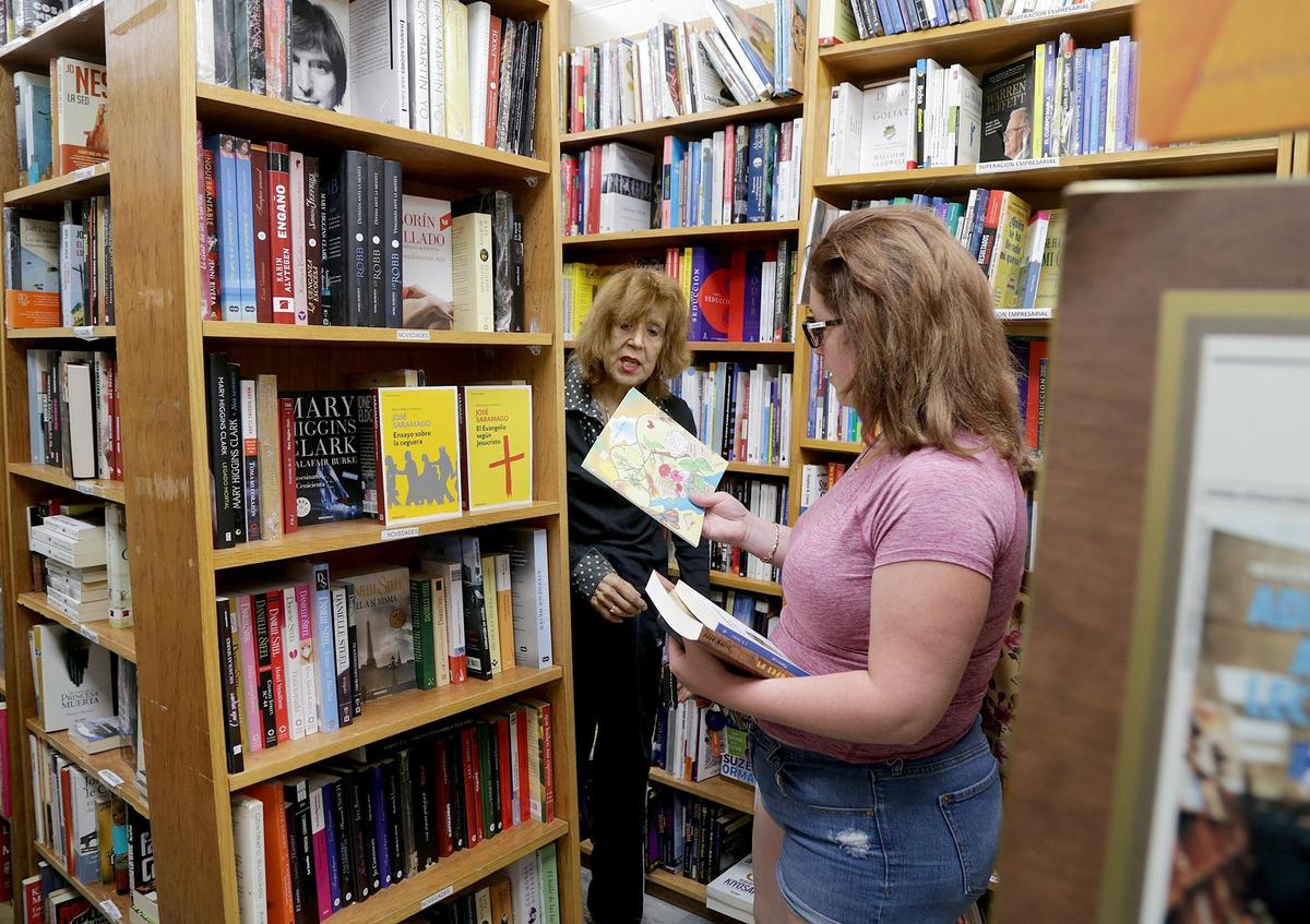 Norma Durán (izq.) asiste a Natalie Valderá, que viene buscando libros en español para sus hijos en la librería Revistas y Periódicos, el 22 de abril.