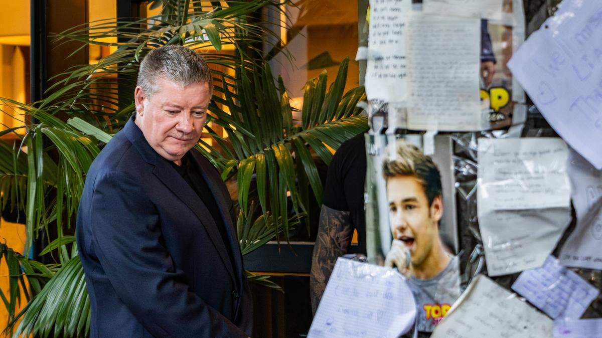 El padre de Liam Payne camina alrededor del altar erigido en homenaje a su hijo. A la derecha, se ve una foto del cantante pegada al árbol en la vereda del hotel junto a cartas y condolencias escritas por fans. 