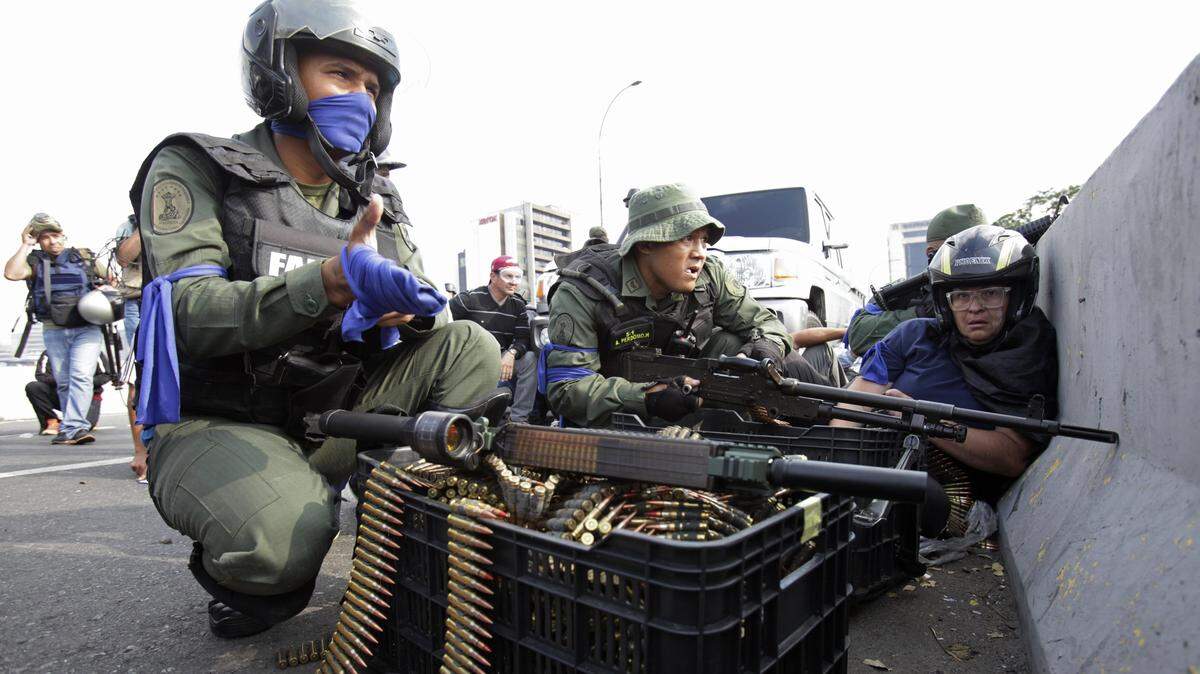 Manifestantes antigubernamentales y soldados rebeldes se protegen el 30 de abril de 2019, cerca de la Base Aérea La Carlota, en Caracas, durante un breve levantamiento contra el gobierno de Nicolás Maduro.