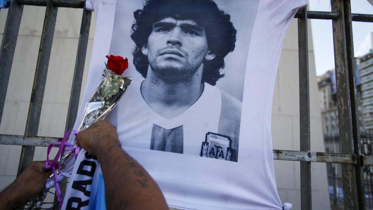 Un hombre coloca una flor en una camiseta con el rostro del fallecido astro del fútbol Diego Maradona durante una marcha para exigir respuestas sobre su muerte, en Buenos Aires, Argentina, el miércoles 10 de marzo de 2021.