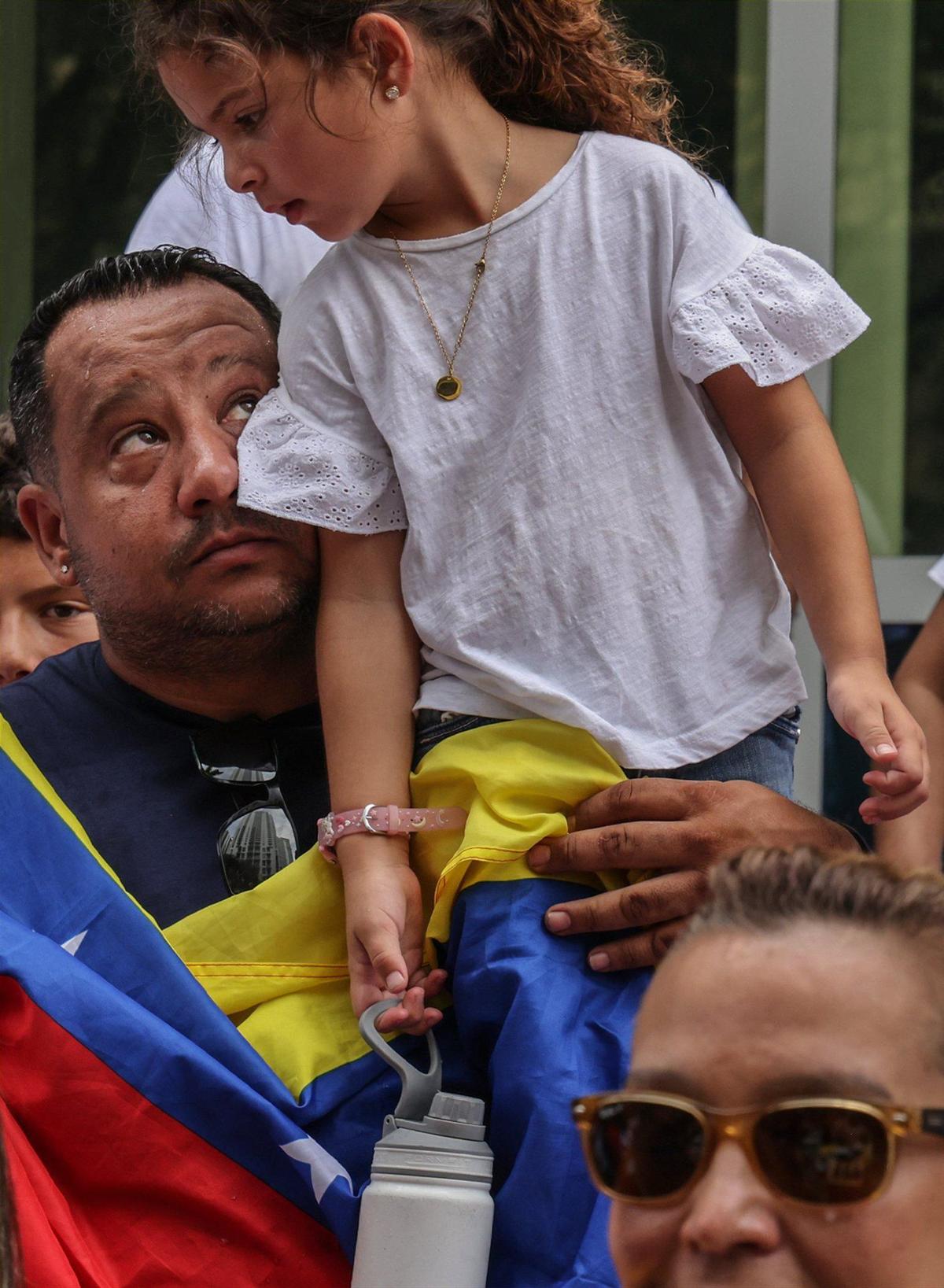 El residente de Davie, Víctor Macedo, de 39 años, a la izquierda, mira a su hija Sonia, de 5 años, sentada en su hombro con esperanza de cambio después de cantar el Himno Nacional de Venezuela durante la manifestación por el derecho a votar en las elecciones venezolanas,las elecciones venezolanas el domingo 28 de julio de 2024 en Miami, Florida.