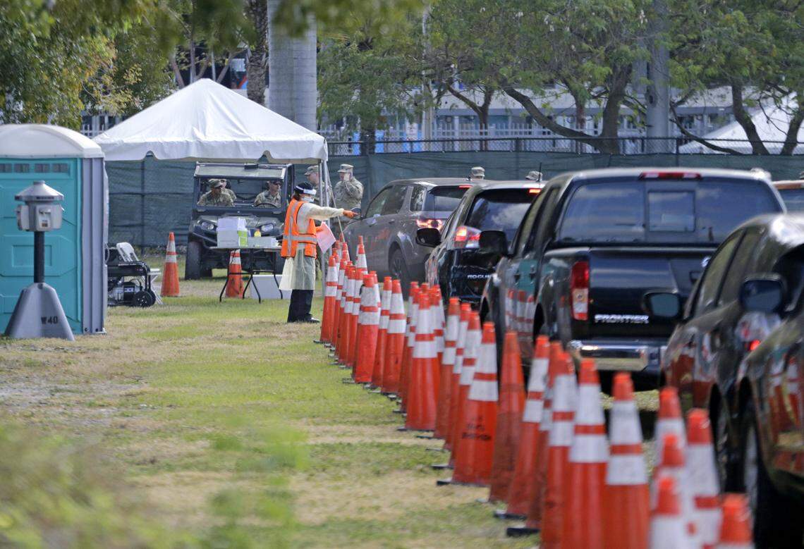 Healthcare workers help to check in with the assistant from the Florida Army National Guard as vehicles line up at COVID-19 at a drive-thru testing center at Marlins Park as the coronavirus pandemic continues on Wednesday, March 25, 2020 in Miami.
