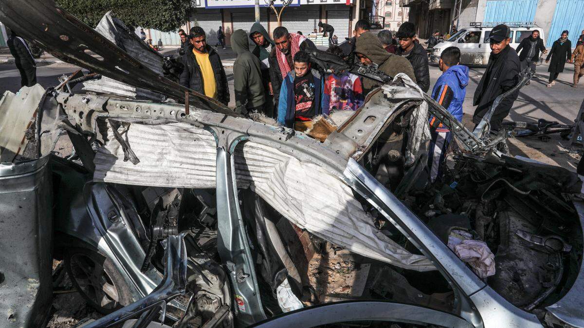 Palestinos examinan un auto destruido en un bombardeo israelí, en Rafah, en el sur de Gaza, el domingo 21 de enero de 2024.