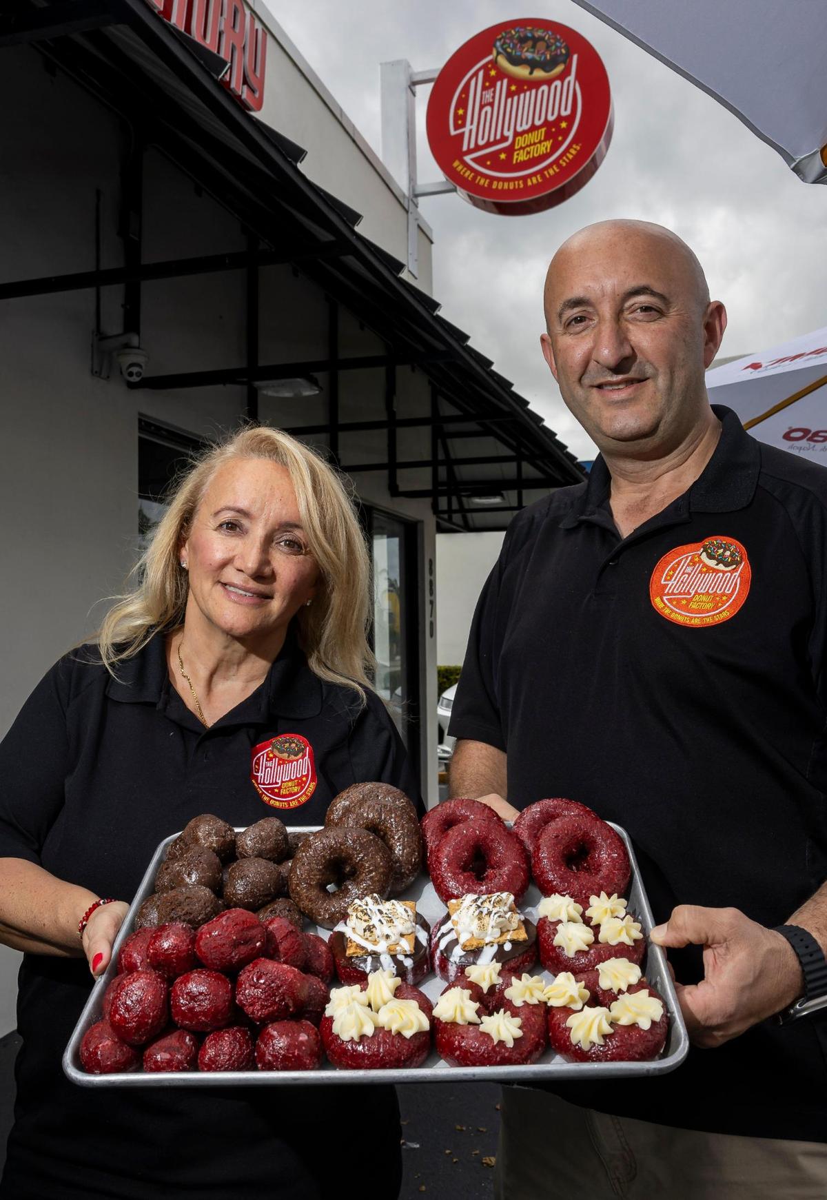 Los propietarios Kat Palushaj y Bobby Palushaj muestran donas de terciopelo rojo y el nuevo letrero de la tienda en Bird Road, en Miami.