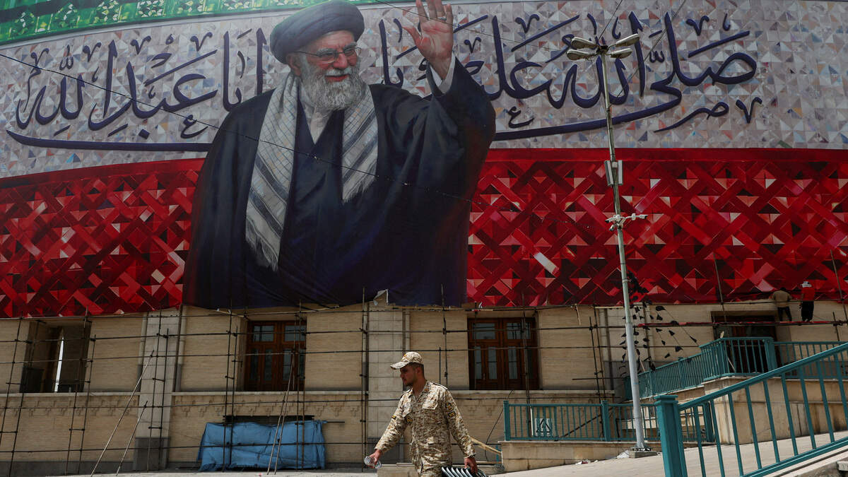 Un miembro de las fuerzas paramilitares Basij lleva piezas metálicas debajo de una gran pancarta que representa al difunto Líder Supremo de Irán, el Ayatolá Ali Jamenei, durante los preparativos para una ceremonia de despedida del difunto Líder Supremo de Irán, quien fue asesinado el 28 de febrero en ataques aéreos israelíes y estadounidenses, en el Gran Mosalla del Imam Jomeini, en Teherán, Irán, el 2 de julio de 2026.
