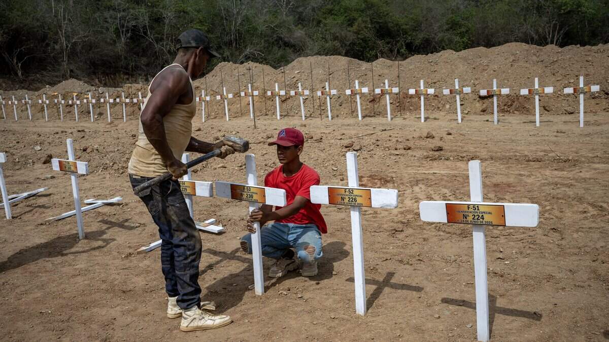 Workers nail a wooden cross onto a freshly dug grave marked with a number at La Esperanza Cemetery in Catia La Mar, La Guaira state, northeast of Caracas on July 5, 2026, where rows of similar graves for unidentified individuals, victims of twin earthquakes, stretch across the site. Venezuela's devastating twin earthquakes killed nearly 3,000, updated official figures showed on July 4, as international rescue teams began winding down search operations for survivors in the rubble of the disaster. (Photo by Miguel MEDINA / AFP via Getty Images)