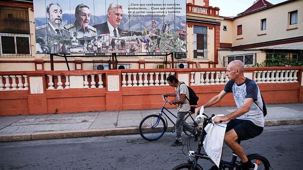 Two men ride bicycles past a billboard depicting the late Cuban leader Fidel Castro, former president Raul Castro, and president Miguel Diaz-Canel in Havana on February 16, 2026. (Photo by YAMIL LAGE / AFP via Getty Images)