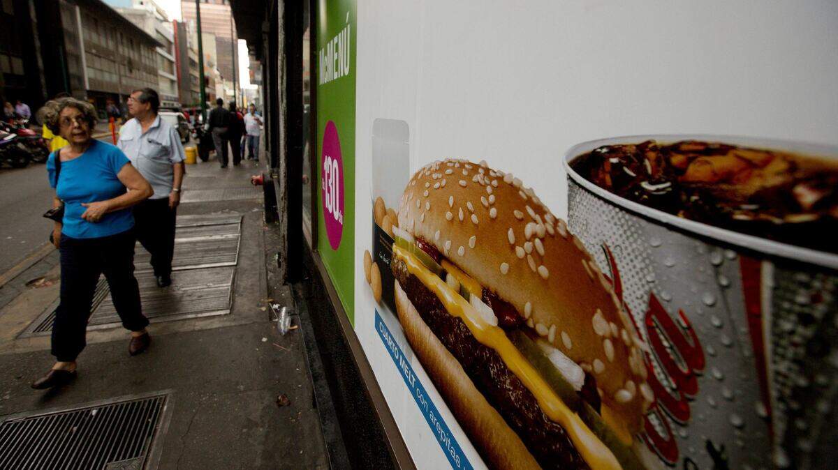 Un cliente en Caracas mira un menú de McDonalds que muestra una hamburguesa acompañada de arepas o pasteles de maíz, en lugar de papas fritas.