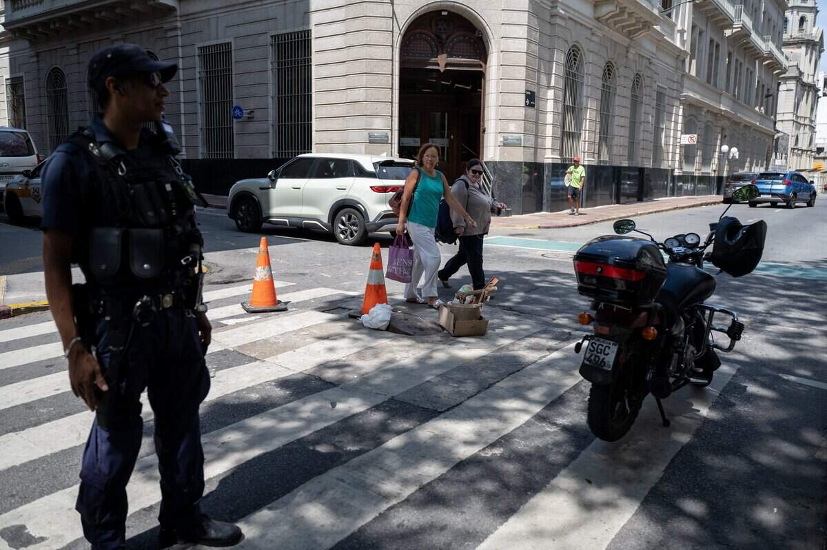 Mujeres cruzan la calle mientras un agente de policía custodia una alcantarilla, un día después de que la policía frustrara un intento de robo a un banco en el que los delincuentes habían excavado un túnel desde un comercio hasta el sistema de alcantarillado, desde donde planeaban ingresar a la entidad financiera, el 3 de febrero de 2026.