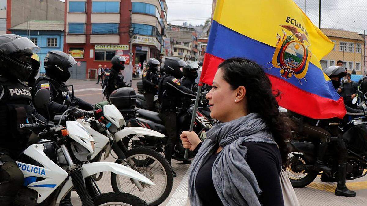 A demonstrator holds an Ecuadorian flag in front of motorcycle-mounted police officers during a march toward El Arbolito park against racism, the criminalization of protest, and in support of the national strike called by CONAIE (Ecuador's largest Indigenous organization) in Quito on October 12, 2025. (Photo by Galo Paguay / AFP) (Photo by GALO PAGUAY/AFP via Getty Images)          