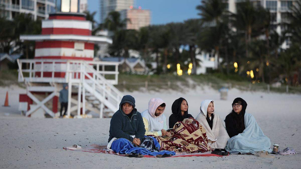 MIAMI BEACH, FLORIDA - NOVEMBER 11: People bundle up against the chilly air as they watch the sunrise on the beach on November 11, 2025 in Miami Beach, Florida. A cool blast of air moved through the area in the morning with temperatures in the upper-40s all across South Florida, and with wind chill it was in the low- to mid-40s. (Photo by Joe Raedle/Getty Images)