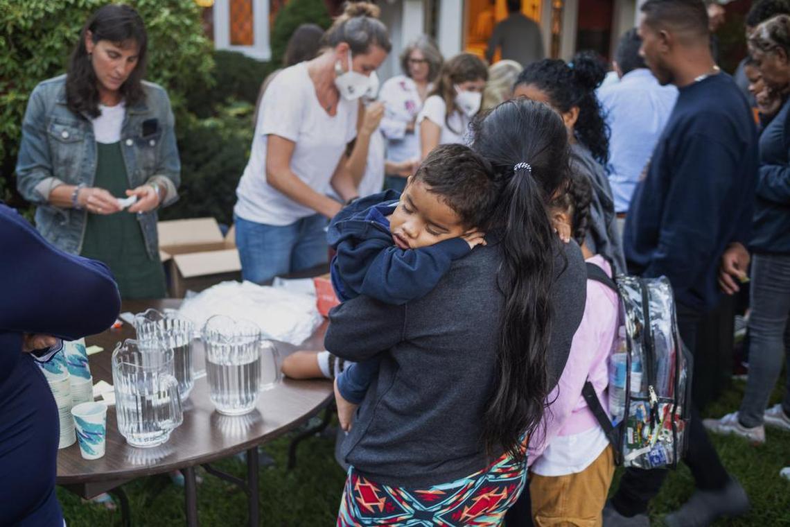 A woman, who is in a group of migrants taken to Martha’s Vineyard, Massachusetts, holds her child as they are fed outside a church. Ray Ewing/Vineyard Gazette/ AP