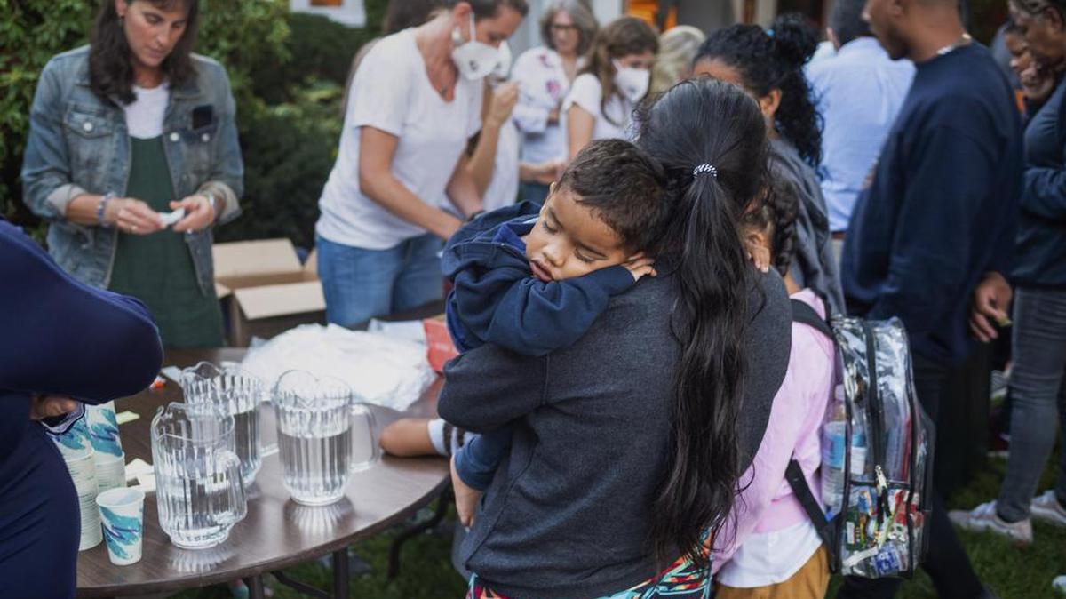 Una mujer, que está en un grupo de migrantes que fueron trasladados en autobús a Martha’s Vineyard, Massachussets, carga a su hijo mientras son alimentados afuera de una iglesia.