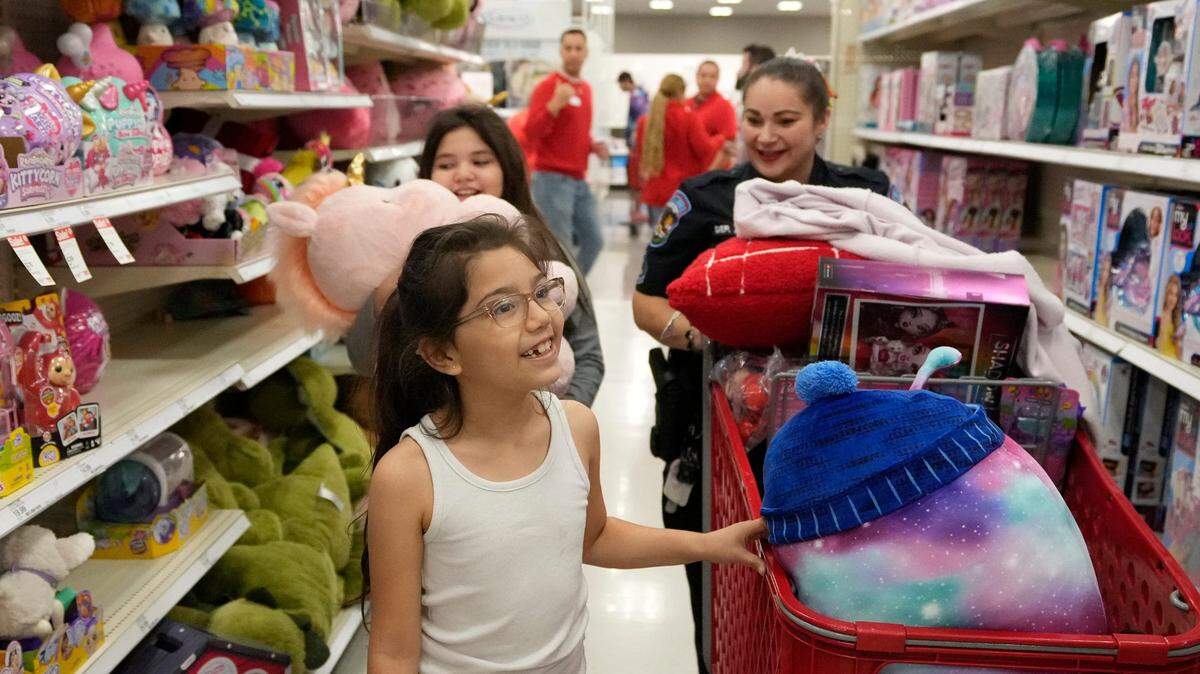 La agente policial Alta Villarreal, del condado Travis, Texas, acompañada por Julisa Saucedo y Azul Solis, ambas de 8 años, realizan compras en una tienda Target en Austin, el 15 de diciembre de 2023. La economía de Estados Unidos creció 3.2% en el cuarto trimestre de 2023 impulsada en gran parte por los consumidores.