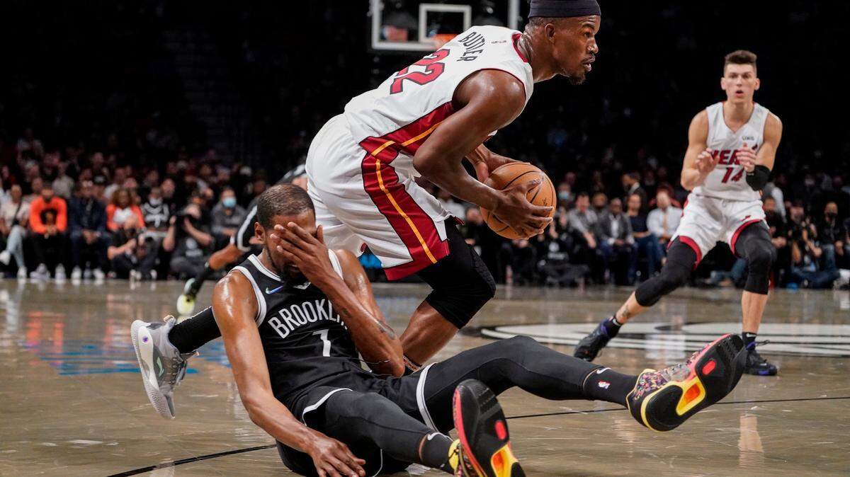 El delantero de los Brooklyn Nets Kevin Durant (7) cae cuando el del Miami Heat Jimmy Butler (22) conduce hacia la canasta, el miércoles 27 de octubre de 2021, en Nueva York.