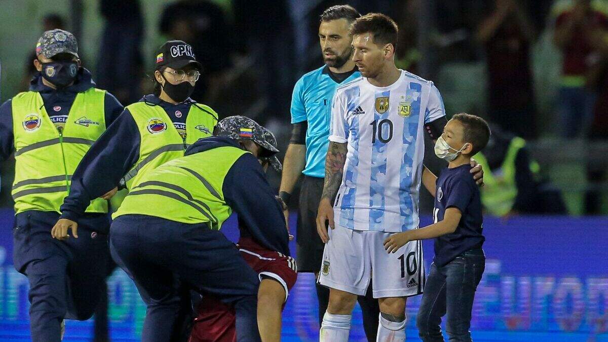 Un niño abraza al argentino Lionel Messi mientras el personal de seguridad inmoviliza a un fanático al finalizar el partido entre Argentina y Venezuela en la eliminatoria mundialista sudamericana, el 2 de septiembre de 2021 en Caracas.
