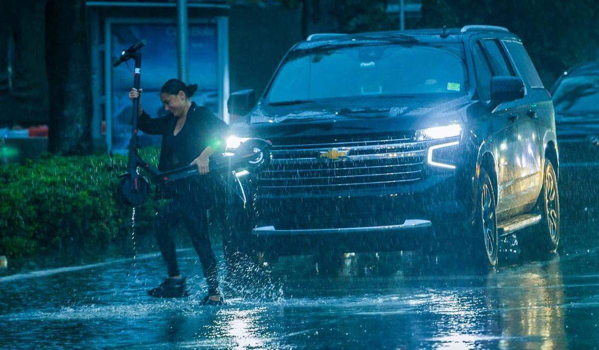 Una mujer carga su scooter bajo una fuerte lluvia mientras cruza Biscayne Boulevard y 14th Street el jueves 13 de junio de 2024. Pedro Portal pportal@miamiherald.com