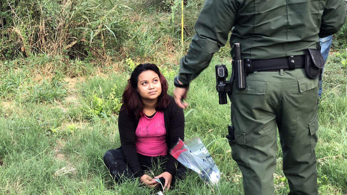Imagen de una mujer detenida en la frontera entre México y Estados Unidos hablando con un policía estadounidense.