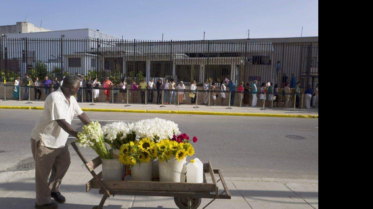 Un vendedor de flores se detiene por un momento a ver la fila de personas en la Embajada de EEUU en La Habana, el 20 de julio. 