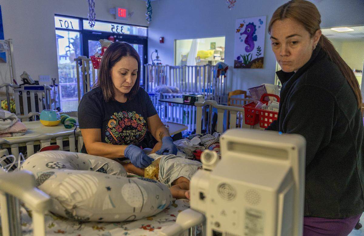 Gladys Martínez (izq), asistente de enfermería certificada, y la enfermera registrada Jamie Turner atienden a uno de los muchos bebés en Patches, un centro de Atención Pediátrica Extendida Prescrita (PPECC).