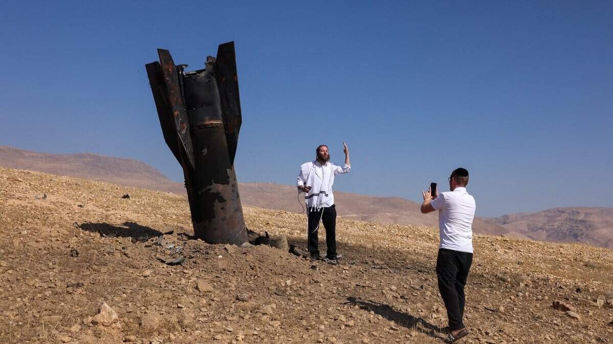 A man poses for a photo next to a fallen rocket half-buried in the ground on the outskirts of Jericho on June 8, 2026, following Iranian and Iran-backed Houthi rebel attacks. Israel and Iran traded fire on June 8, seriously testing a fragile truce and threating hopes for a deal to end the Middle East war. (Photo by AHMAD GHARABLI / AFP via Getty Images) / 