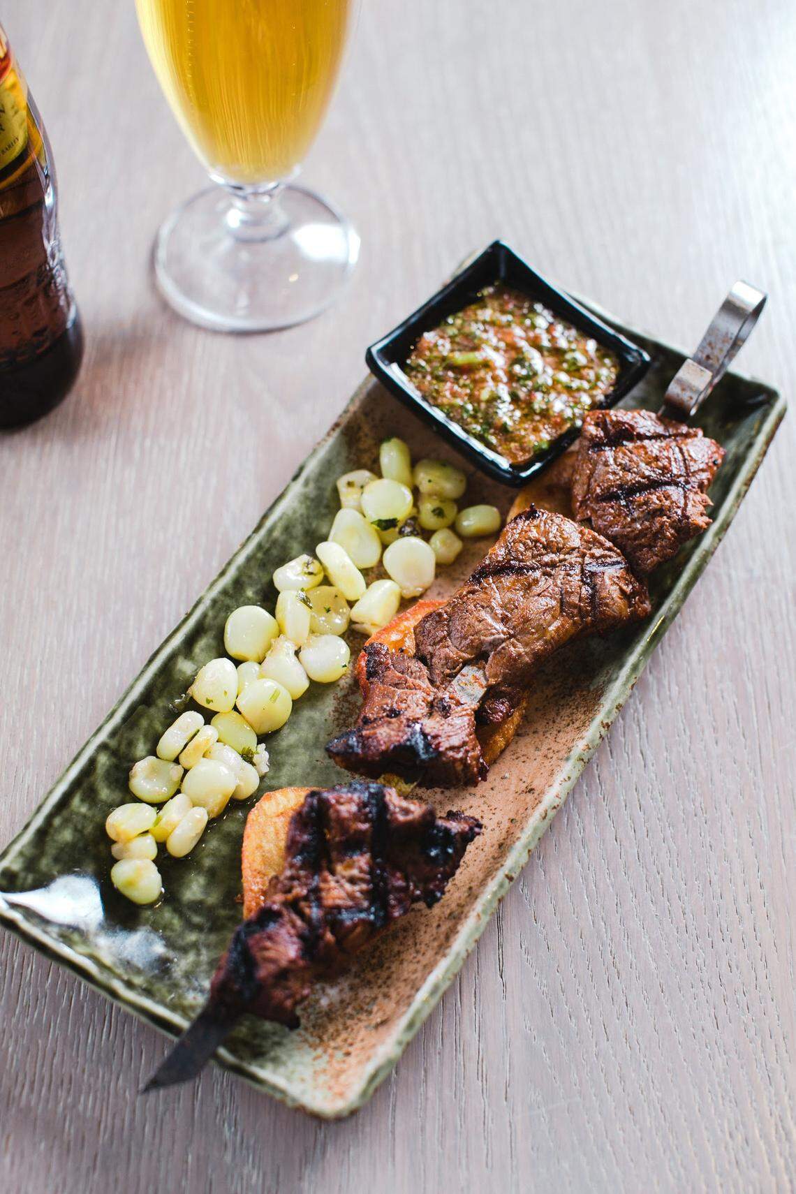 Anticucho de carne, una riquísima brocheta de lomo de res asado con papas, cholo y salsas anticuchera y ají de la casa.