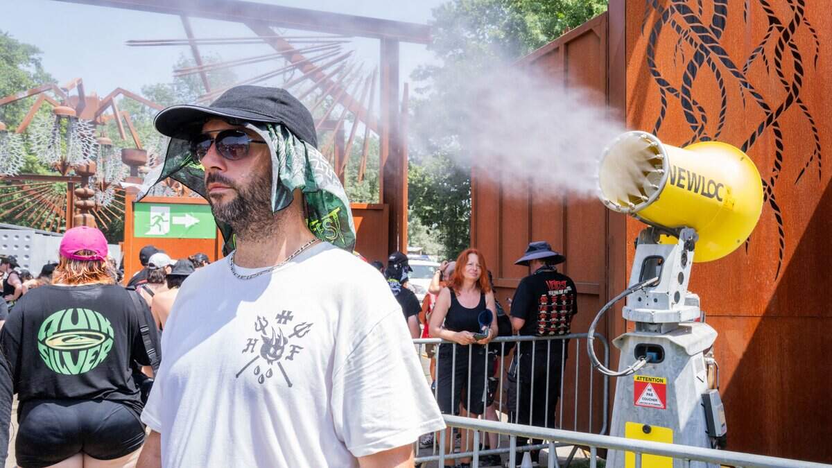 Festivalgoers pass under a water spray to cool down during the heatwave at the Hellfest festival site in Clisson, Loire-Atlantique, France, June 21, 2026. The image highlights one of the consequences of the extreme heat at the metal festival, as visitors seek refreshment and relief from high temperatures. (Photo by Jimmy Beunardeau / Hans Lucas / AFP via Getty Images)