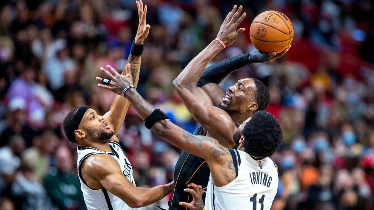 El centro de los Miami Heat, Bam Adebayo (13), dispara sobre el armador de los Brooklyn Nets, Kyrie Irving (11) y el alero Bruce Brown (2), durante el tercer cuarto de un partido de la NBA en el FTX Arena en el centro de Miami, Florida, el sábado 12 de febrero de 2022.