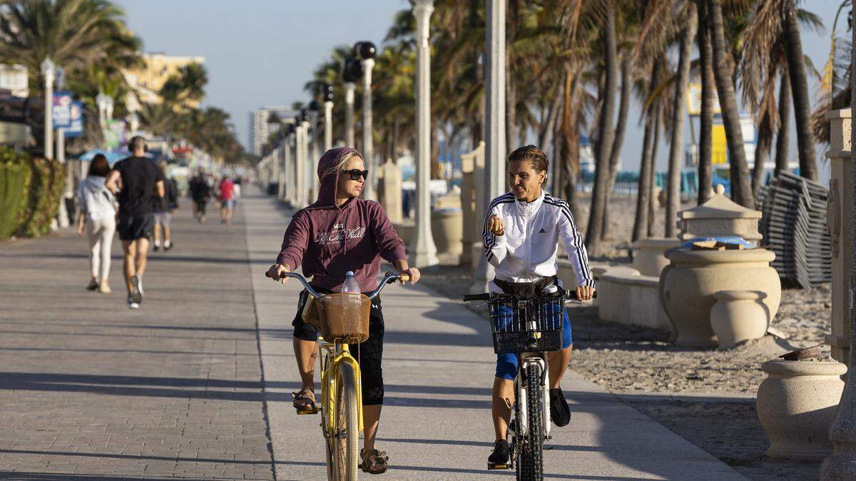 Christie Sadowski, a la izquierda, y Andi Bredak recorren en bicicleta el Hollywood Beach Broadwalk mientras las temperaturas caen el martes 28 de noviembre de 2023, en Hollywood, Florida.