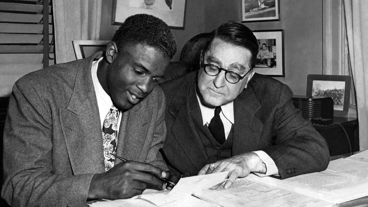 Jackie Robinson firma un nuevo contrato con los Dodgers de Brooklyn con la presencia de Branch Rickey, presidente del equipo, el 12 de febrero de 1948.